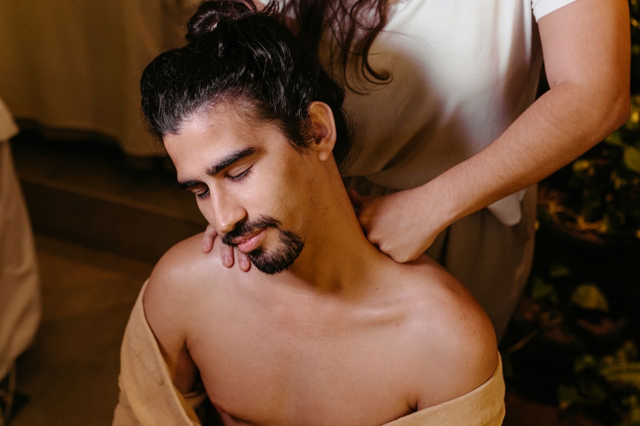 A serene spa scene showing a man receiving a therapeutic shoulder massage indoors.